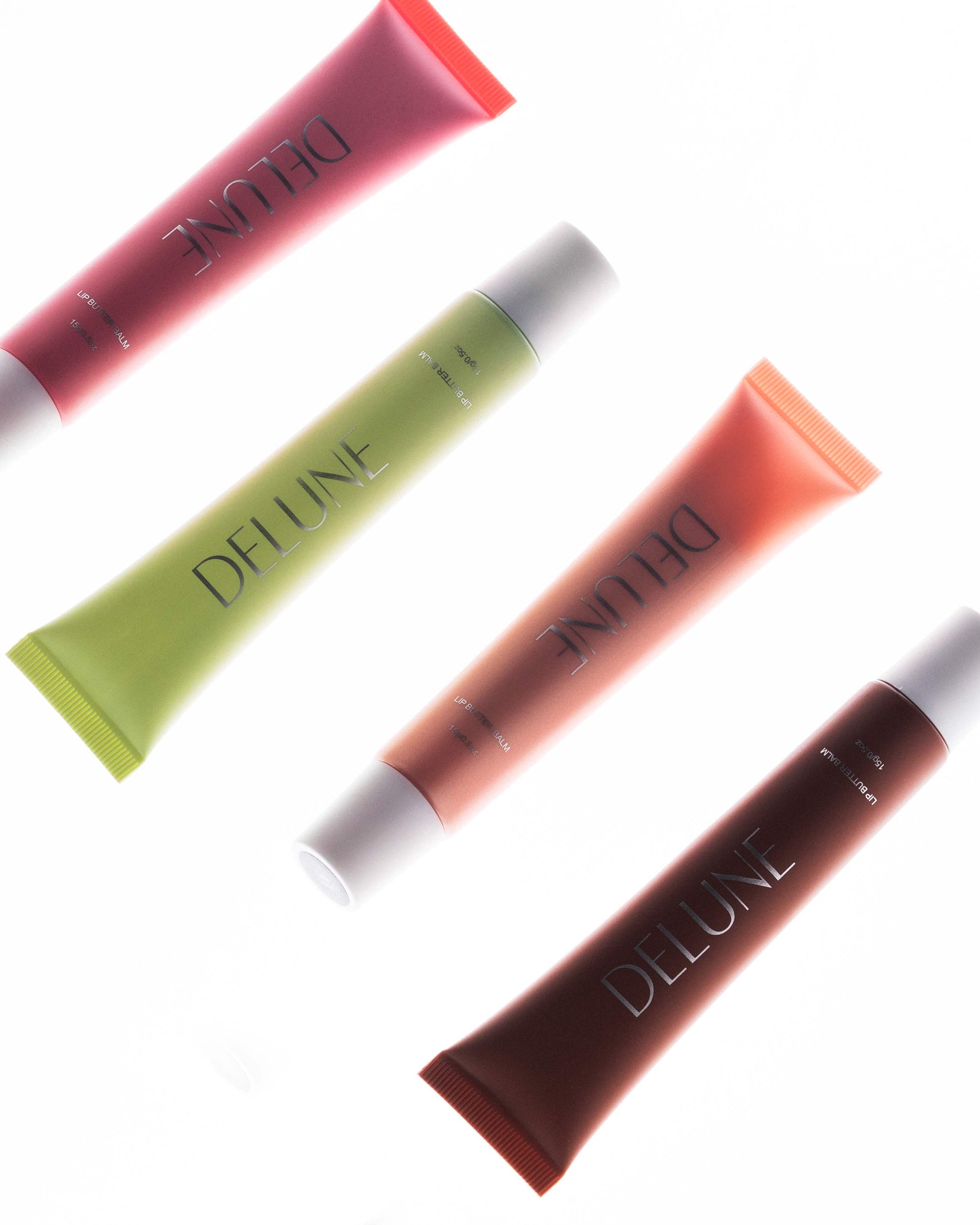 Quatre teintes de Lip Butter Balm Delune accompagnées d’échantillons brillants