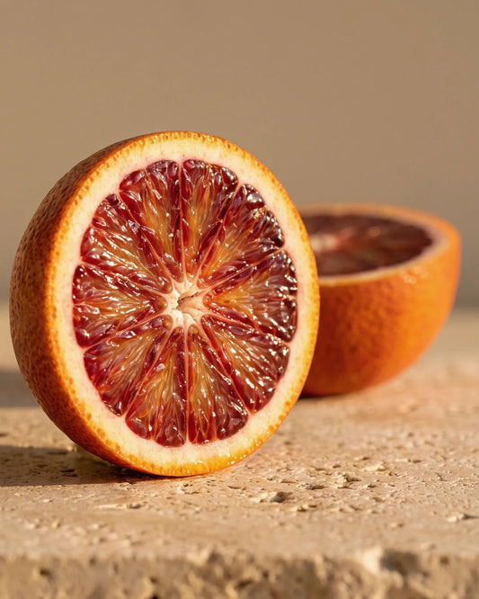 Orange sanguine coupée en deux, à la chair rubis profond, sur travertin chaud : la senteur hespéridée, douce et fruitée de l’huile essentielle pure d’orange sanguine Delune