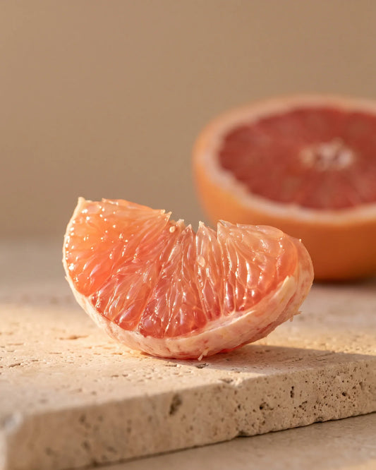Quartier de pamplemousse rose scintillant en contre-jour sous un soleil chaud : la senteur douce-amère et juteuse de l’huile essentielle pure de pamplemousse rose Delune