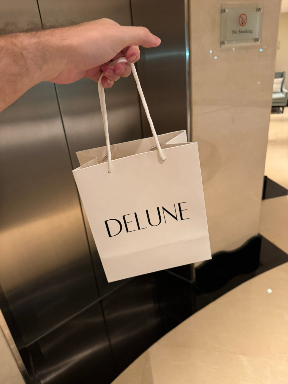 Une main tient un sac-cadeau blanc Delune, en route pour livrer une commande