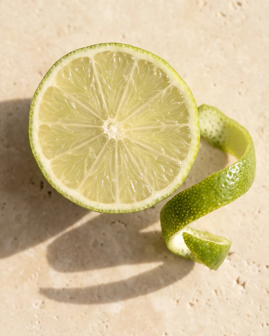 Lime fraîche coupée en deux et zeste de lime vus de dessus sur travertin chaud : la senteur vive et zestée de l’huile essentielle pure de lime Delune