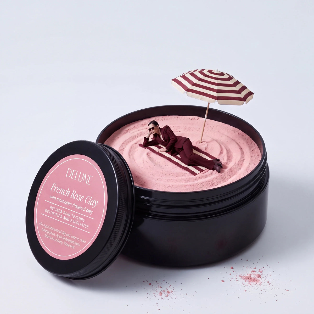 Rituel : une femme en tailleur bordeaux se prélasse sous un parasol sur de l’argile rose, dans un pot géant d’argile rose française Delune